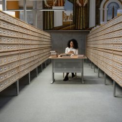a girl sitting in front of a table between database wooden drawer